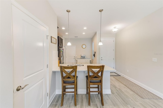 kitchen featuring sink, decorative light fixtures, kitchen peninsula, a breakfast bar, and stainless steel fridge