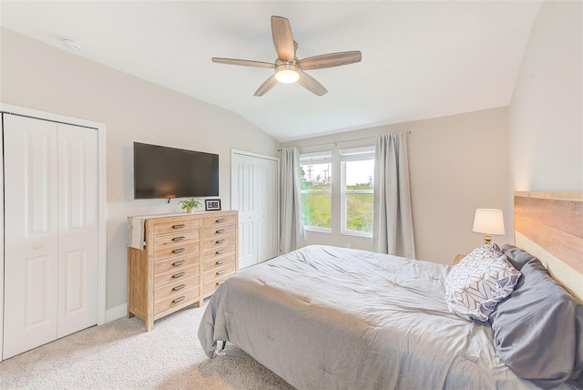 bedroom with ceiling fan, two closets, light colored carpet, and vaulted ceiling