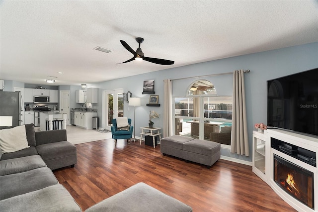 living room featuring ceiling fan, dark hardwood / wood-style flooring, and a textured ceiling