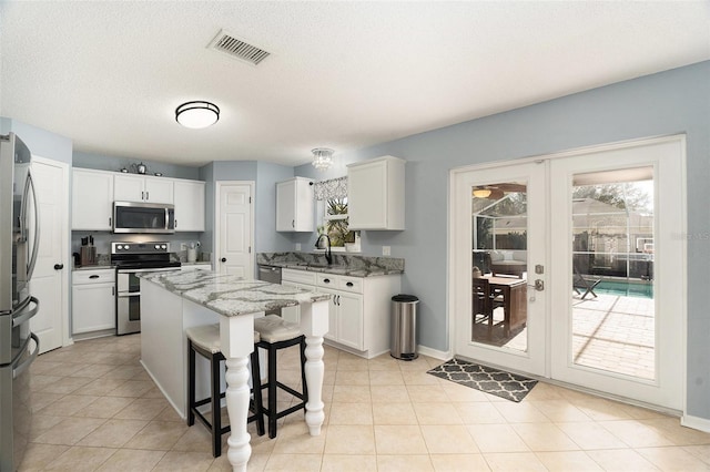 kitchen featuring a center island, french doors, white cabinets, appliances with stainless steel finishes, and light stone counters