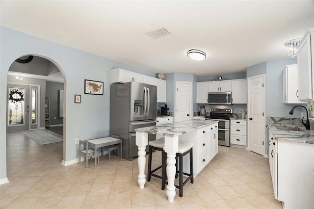 kitchen featuring a center island, white cabinets, sink, light stone countertops, and stainless steel appliances