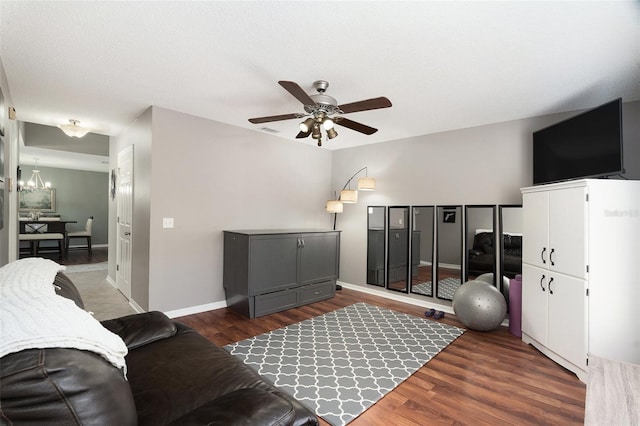 living room featuring ceiling fan with notable chandelier and dark wood-type flooring