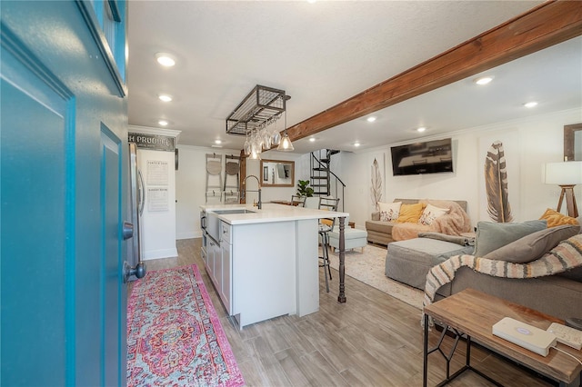 kitchen with pendant lighting, sink, a kitchen island with sink, light hardwood / wood-style flooring, and beam ceiling