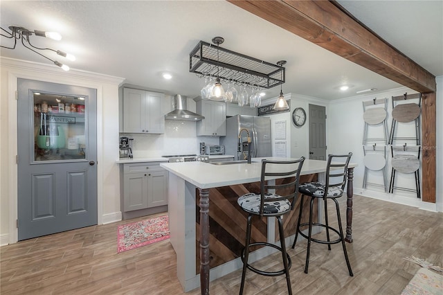 kitchen featuring decorative light fixtures, wall chimney range hood, gray cabinets, light wood-type flooring, and a kitchen island with sink