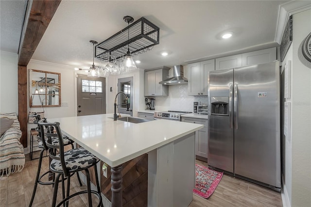 kitchen featuring a center island with sink, stainless steel appliances, wall chimney range hood, crown molding, and a breakfast bar