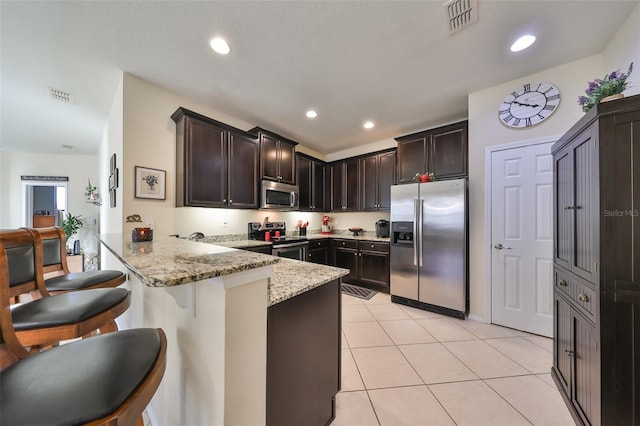 kitchen featuring a breakfast bar, light stone countertops, light tile patterned flooring, kitchen peninsula, and stainless steel appliances