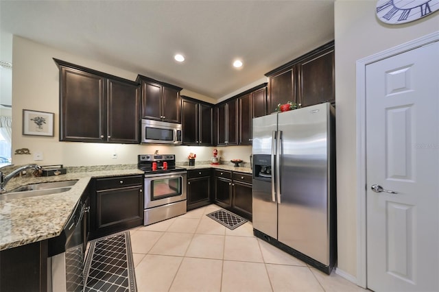 kitchen with appliances with stainless steel finishes, light stone counters, dark brown cabinets, and sink