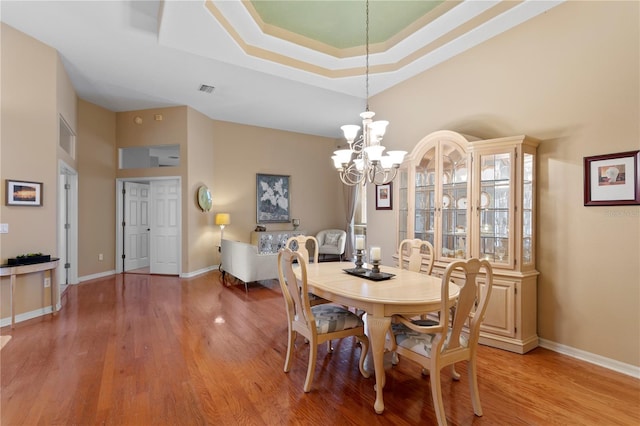 dining space featuring a raised ceiling, light hardwood / wood-style floors, and an inviting chandelier