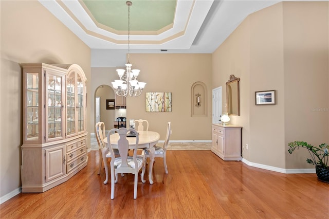 dining area with light hardwood / wood-style floors, a raised ceiling, a towering ceiling, and an inviting chandelier