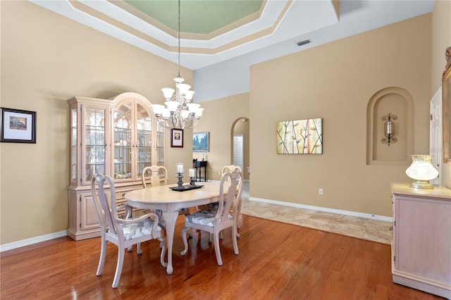 dining space with a high ceiling, light wood-type flooring, a tray ceiling, and an inviting chandelier