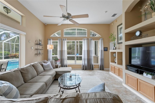 living room with built in shelves, ceiling fan, and plenty of natural light