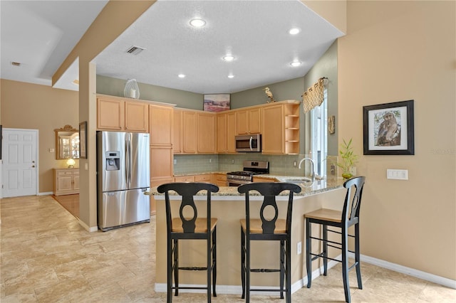 kitchen with kitchen peninsula, appliances with stainless steel finishes, a kitchen bar, light stone counters, and light brown cabinets