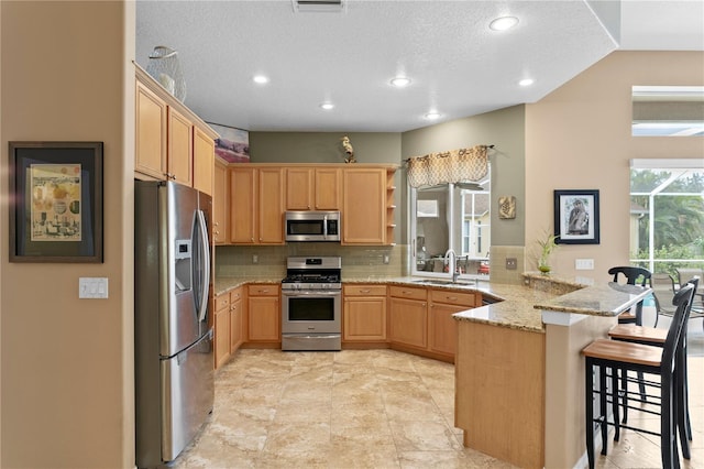 kitchen featuring kitchen peninsula, appliances with stainless steel finishes, decorative backsplash, light stone countertops, and a kitchen breakfast bar