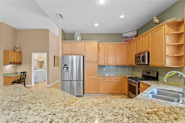 kitchen with light stone countertops, independent washer and dryer, stainless steel appliances, and sink