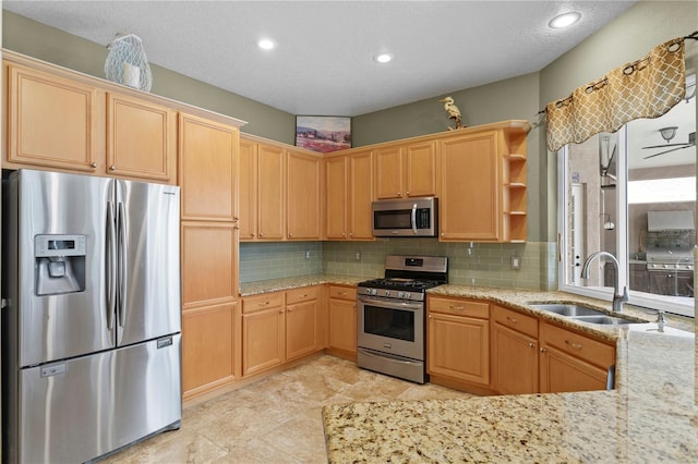 kitchen with decorative backsplash, light stone counters, sink, and appliances with stainless steel finishes