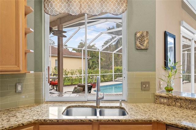 kitchen with tasteful backsplash, light stone counters, plenty of natural light, and sink