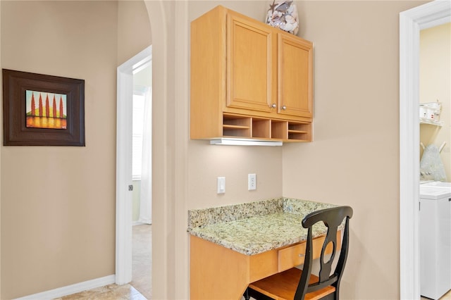 kitchen featuring light stone countertops, washer / dryer, light brown cabinetry, light tile patterned flooring, and built in desk