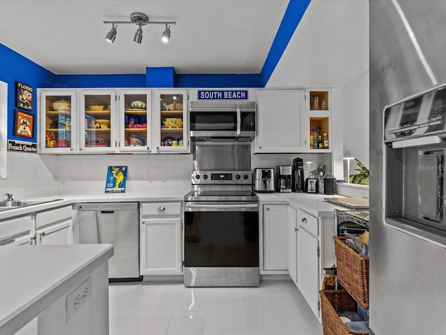 kitchen with tasteful backsplash, white cabinets, light tile patterned floors, and stainless steel appliances