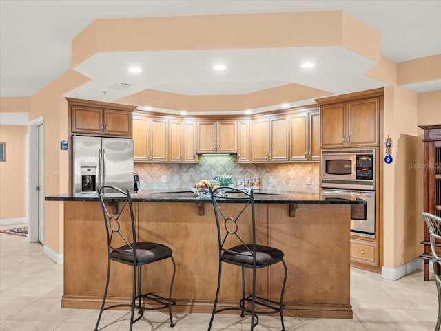 kitchen with appliances with stainless steel finishes, dark stone counters, decorative backsplash, and a breakfast bar area