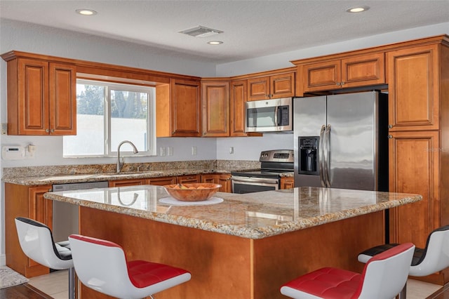 kitchen with light stone countertops, sink, stainless steel appliances, a textured ceiling, and a kitchen bar