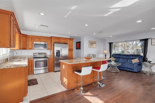 kitchen with sink, light stone countertops, light hardwood / wood-style floors, a kitchen island, and stainless steel appliances