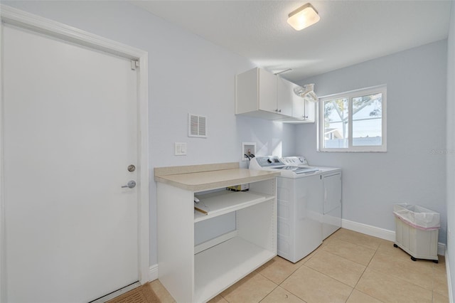 clothes washing area with cabinets, light tile patterned floors, and washing machine and clothes dryer