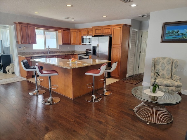 kitchen with stainless steel appliances, a breakfast bar, dark wood-style flooring, a sink, and a center island