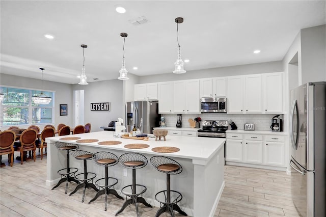 kitchen featuring appliances with stainless steel finishes, pendant lighting, a center island with sink, white cabinets, and a breakfast bar area