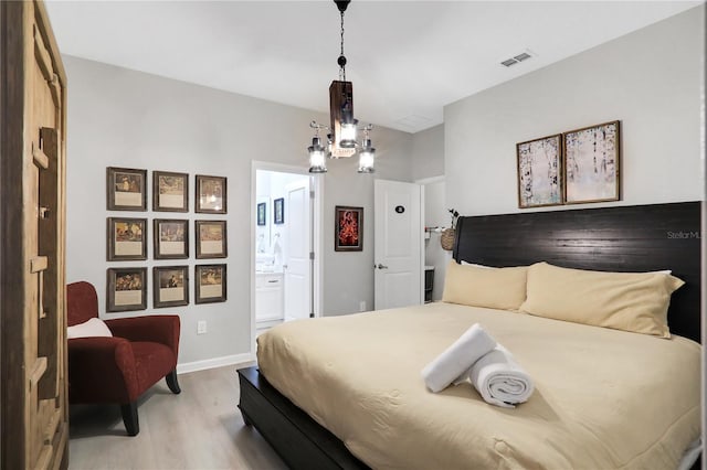 bedroom with a chandelier, light wood-type flooring, and ensuite bathroom