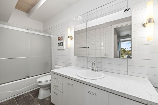 full bathroom featuring vanity, shower / bath combination with glass door, tile patterned floors, toilet, and tile walls