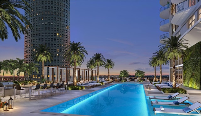 pool at dusk with area for grilling and a patio area