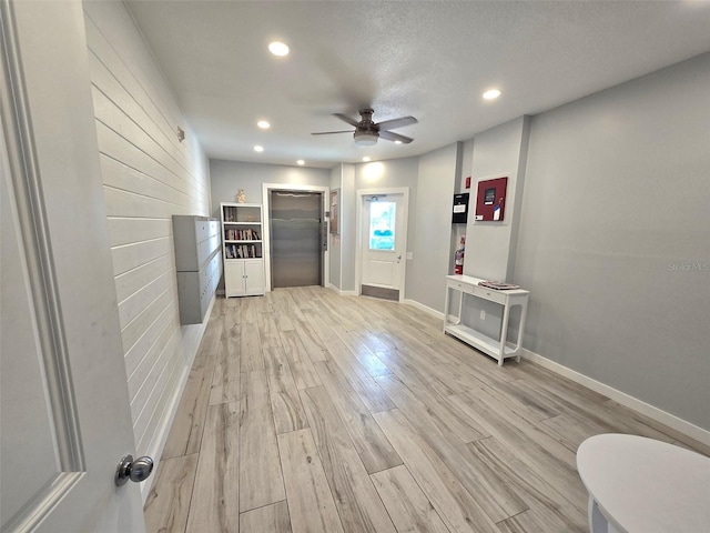 interior space featuring ceiling fan, a textured ceiling, light hardwood / wood-style floors, and elevator