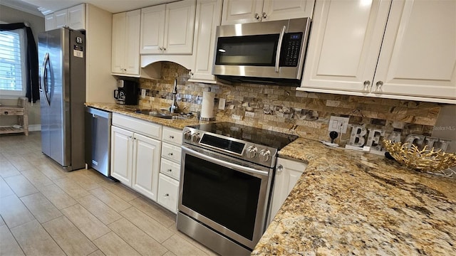 kitchen with appliances with stainless steel finishes, tasteful backsplash, sink, white cabinets, and light stone countertops