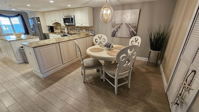 kitchen with appliances with stainless steel finishes, backsplash, a center island, light stone countertops, and decorative light fixtures