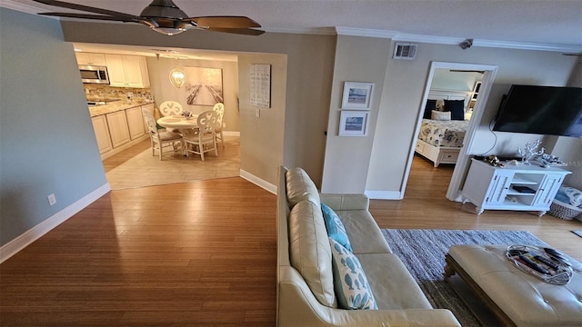 living room featuring ornamental molding, ceiling fan, and light wood-type flooring