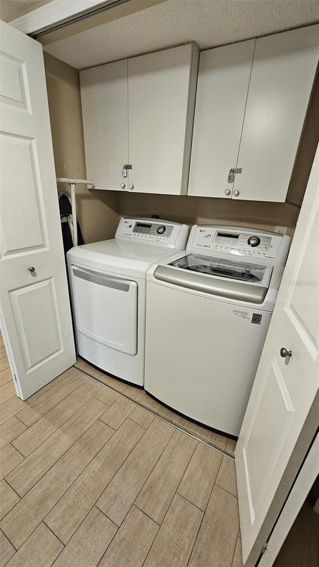 clothes washing area with cabinets, a textured ceiling, and independent washer and dryer