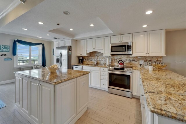 18325 Gulf Blvd Unit 407, Redington Shores, FL 33708 - kitchen with appliances with stainless steel finishes, a sink, a tray ceiling, decorative backsplash, and white cabinetry