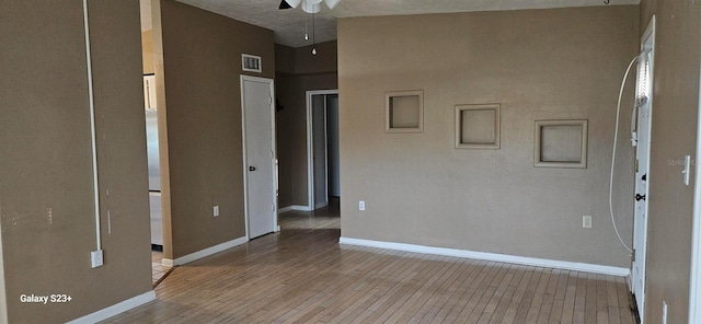 unfurnished room with a towering ceiling, a textured ceiling, light hardwood / wood-style flooring, and ceiling fan