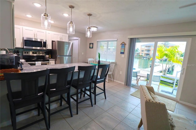 kitchen featuring appliances with stainless steel finishes, a kitchen breakfast bar, light tile patterned floors, pendant lighting, and white cabinetry