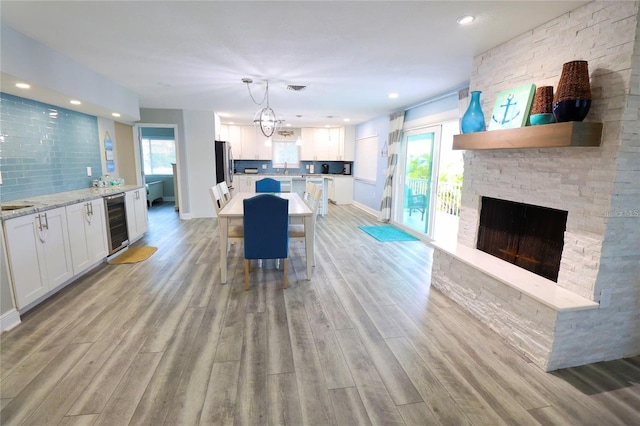 living room with a stone fireplace, a wealth of natural light, wine cooler, and light wood-type flooring