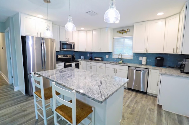 kitchen with decorative light fixtures, a kitchen bar, white cabinetry, and stainless steel appliances