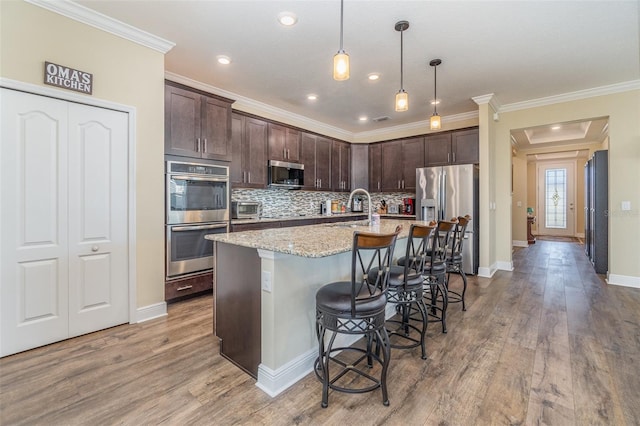 kitchen with a breakfast bar, a center island with sink, sink, light stone countertops, and stainless steel appliances