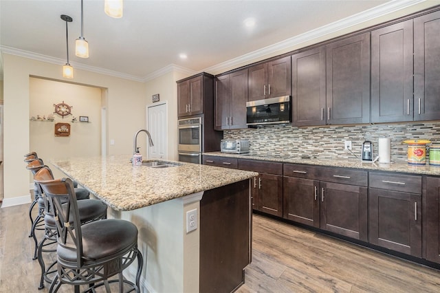 kitchen featuring sink, an island with sink, decorative light fixtures, light stone counters, and stainless steel appliances