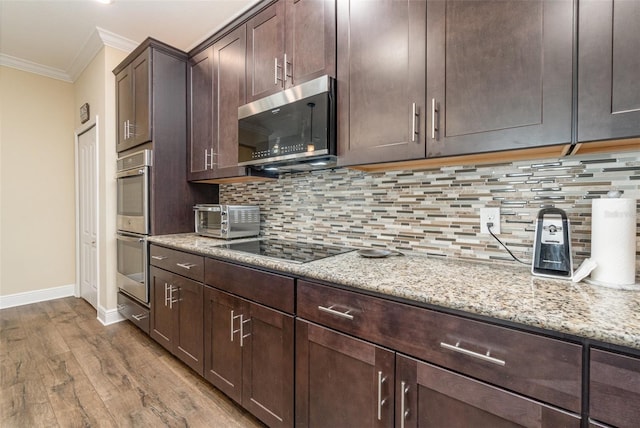 kitchen with decorative backsplash, light stone counters, dark brown cabinetry, stainless steel appliances, and crown molding