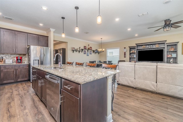 kitchen featuring a breakfast bar, stainless steel appliances, a kitchen island with sink, sink, and decorative light fixtures