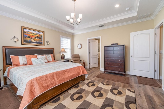 bedroom with a raised ceiling, ornamental molding, a notable chandelier, and hardwood / wood-style flooring