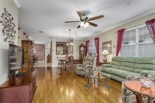 living room featuring ornamental molding, ceiling fan with notable chandelier, light hardwood / wood-style flooring, and a tray ceiling