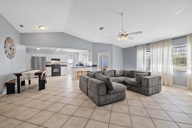 living room with vaulted ceiling, ceiling fan, light tile patterned floors, and a textured ceiling