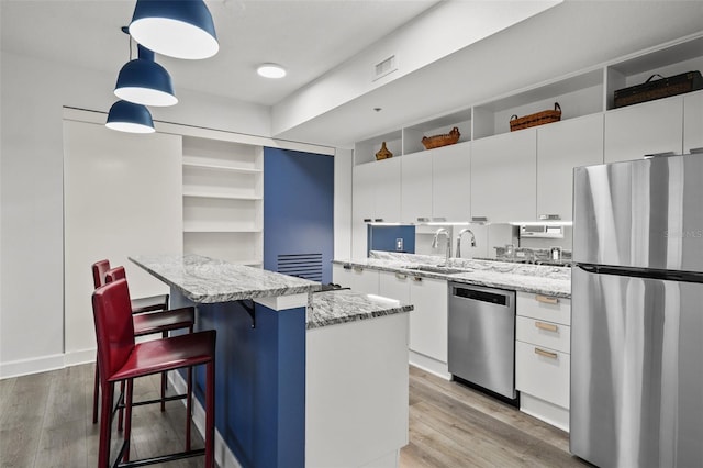 kitchen featuring stainless steel appliances, a center island, white cabinetry, and decorative light fixtures