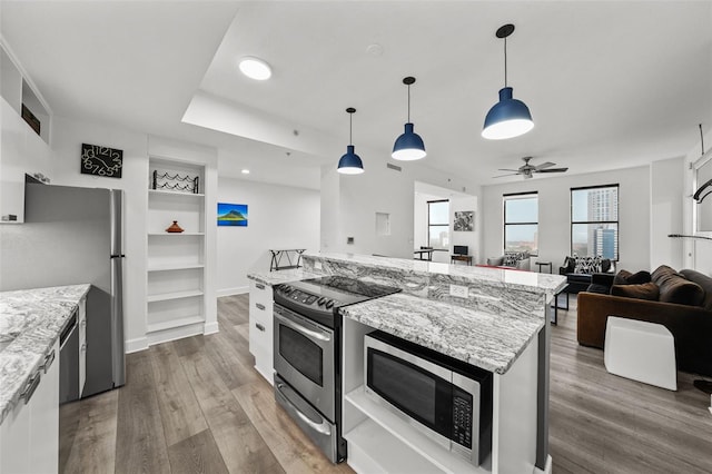 kitchen with decorative light fixtures, a center island, white cabinetry, light stone countertops, and appliances with stainless steel finishes